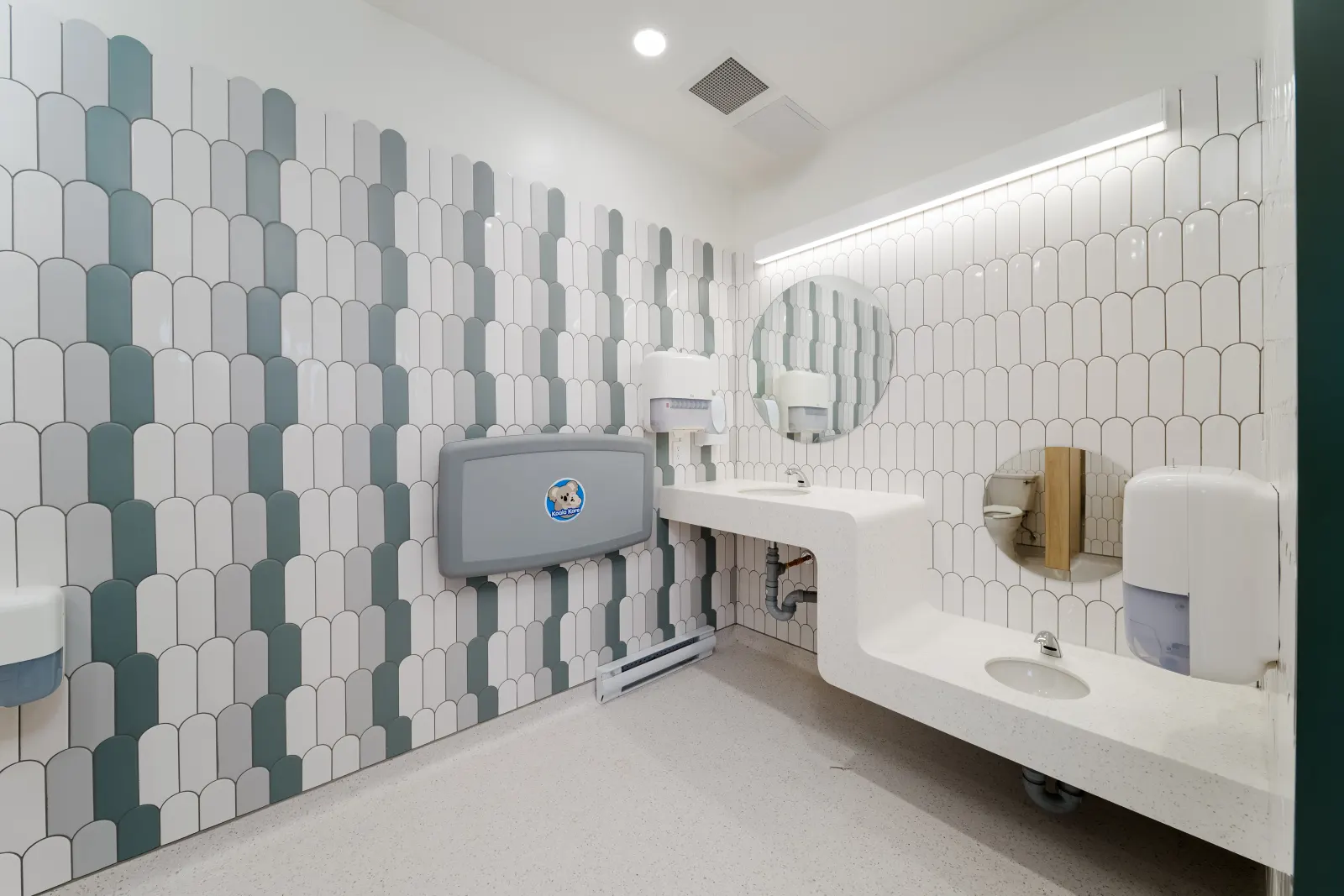 Washroom with scalloped white and green tile, a wall-mounted change table and a stepped solid-surface sink counter